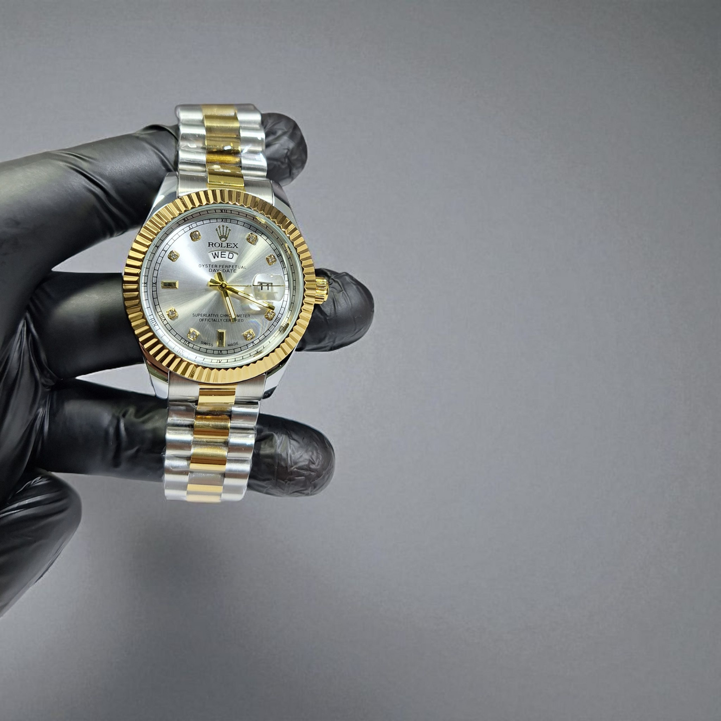Gold and silver watch held by a gloved hand against a gray background