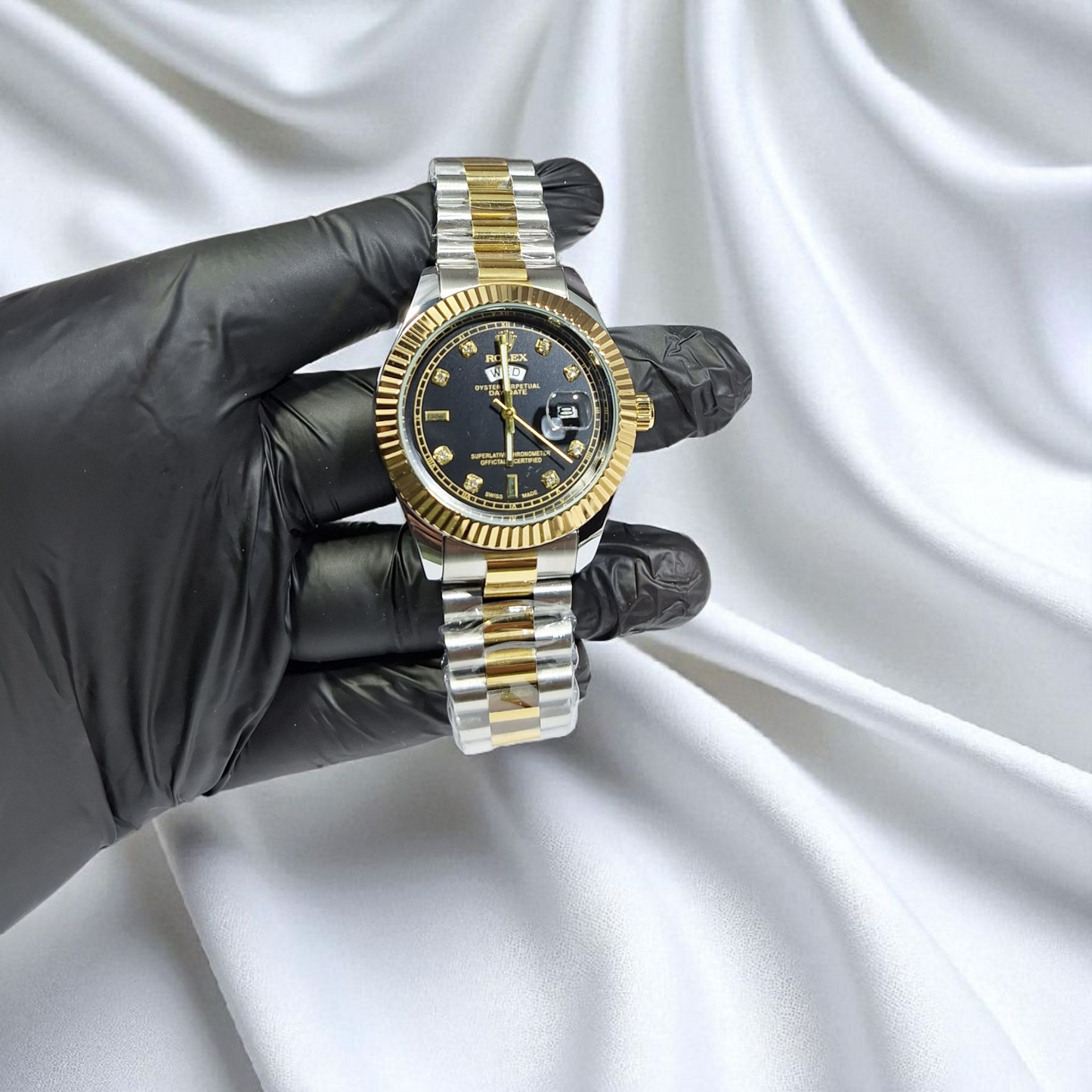 Gold and silver watch held by a gloved hand against a white fabric background