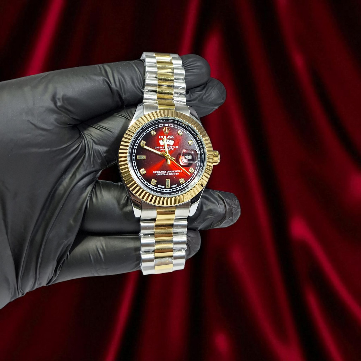 Gold and silver watch held by a gloved hand against a red curtain background
