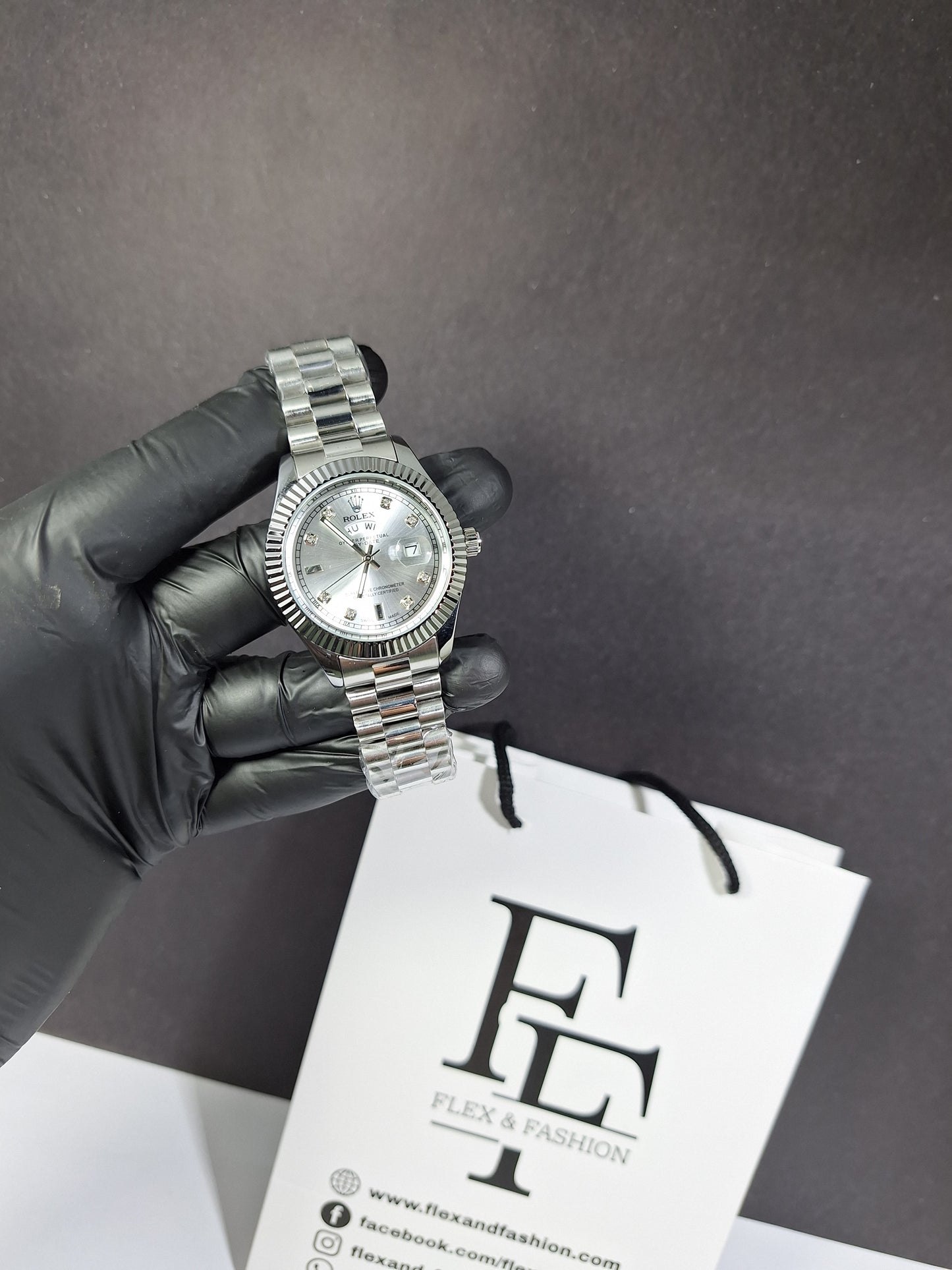 Silver watch held by a gloved hand with a branded box in the background